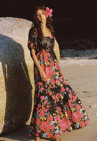 A woman stands barefoot on a sandy beach beside a large rock